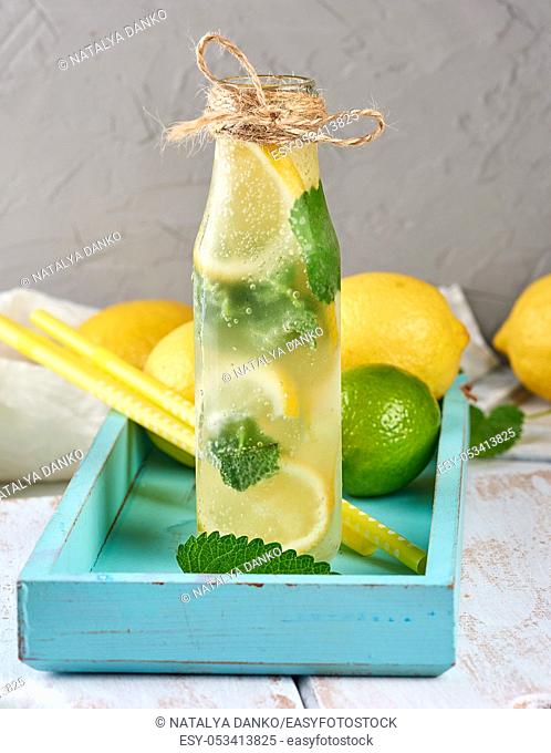 cold drink with lemons, mint leaves, lime in a glass bottle, near the ingredients for making lemonade