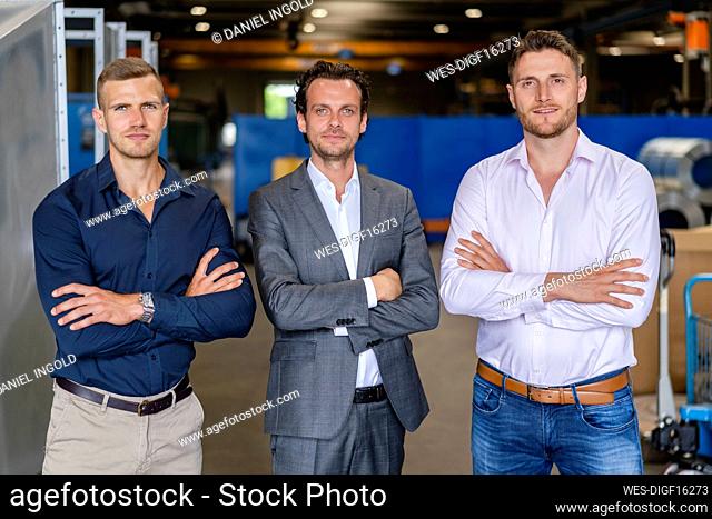 Confident male professionals standing with arms crossed in factory