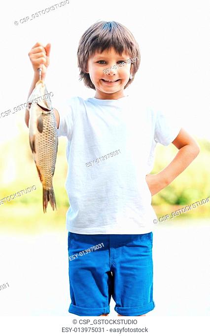 I catch it by myself! Happy little boy carrying big fish on the hook and smiling while standing at the riverbank
