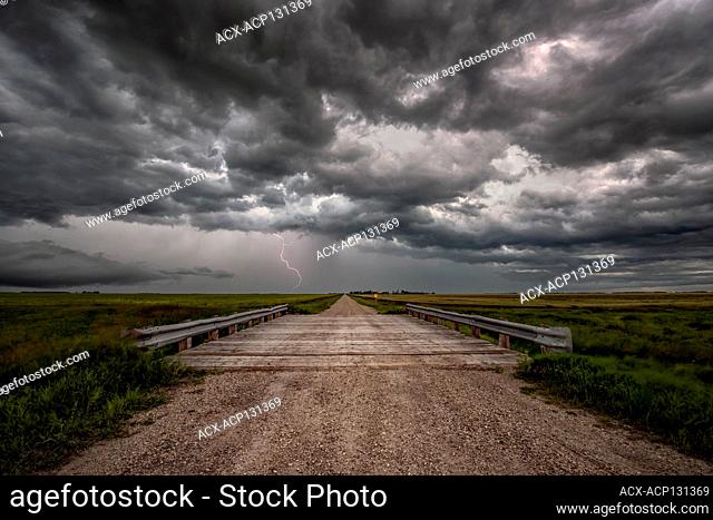 Storm with lightning flashing over old rural bridge on gravel road in rural southern Manitoba Canada