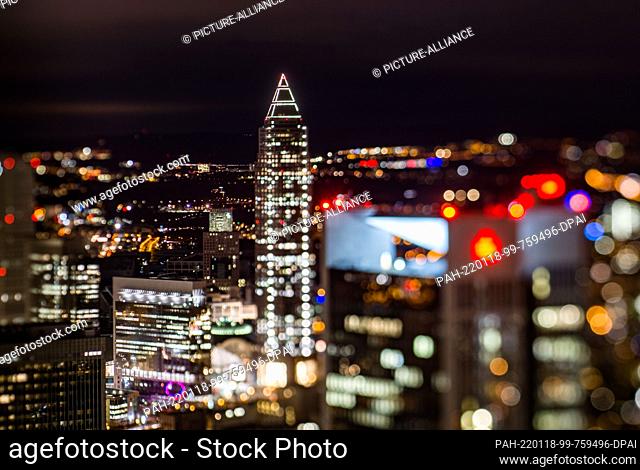 dpatop - 18 January 2022, Hessen, Frankfurt/Main: The Messeturm stands between the lights of the other high-rise and residential buildings (shot with tilt-shift...