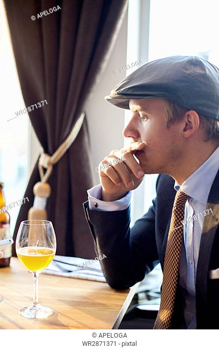 Thoughtful young gay man sitting with hand on mouth at table in restaurant