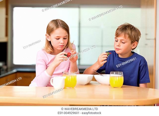 Cute children eating strawberries for breakfast