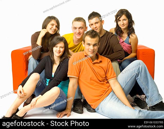 Group of 6 teenagers sitting on and next to the red couch. They're smiling and looking at camera