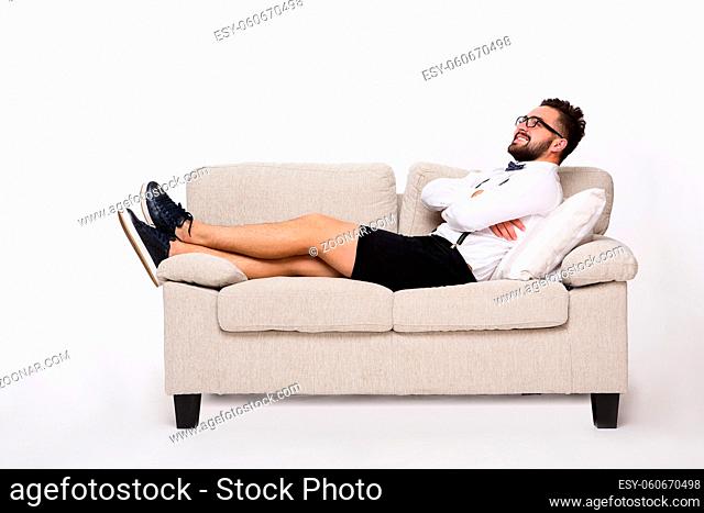 Picture of smiling handsome hipster man lying on couch or sofa and looking upwards. Young man lying with his arms crossed or folded isolated on white background
