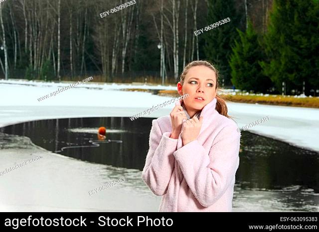 Pretty girl in pink coat near artificial lake in winter forest