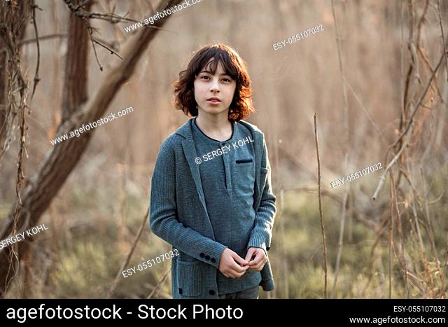 Portrait of a handsome fashionable boy, dressed in jeans and a knitted sweater on a background of nature