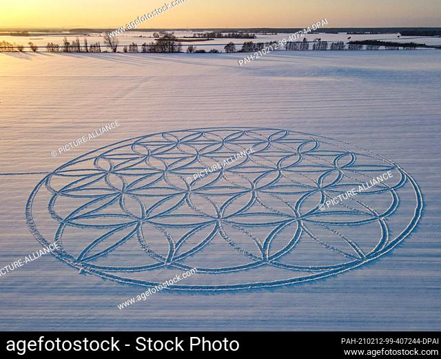 10 February 2021, Brandenburg, Jacobsdorf: The sunset shines over the symbol ""Flower of Life"", which can be seen as a huge pattern in the snow (aerial view...