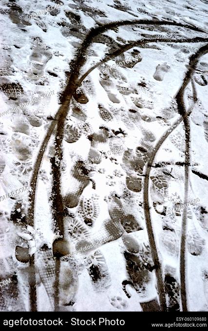 Schuhabdrücke sowie Fahrradreifenabdrücke auf der dünnen Schneedecke eines Gehweges