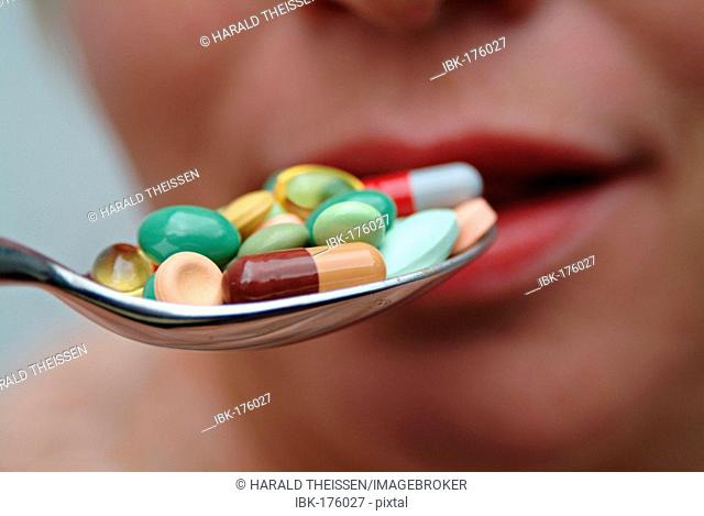Spoon filled with many different colourful pills and capsules getting into a mouth