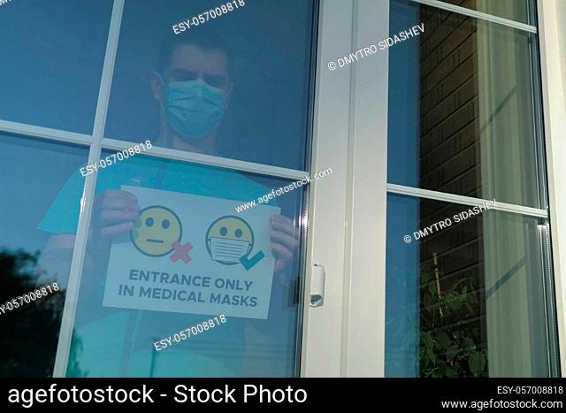 Concept of mandatory wearing of medical masks during the COVID-19 pandemic. Man hangs an ad on the door: ENTRANCE ONLY IN MEDICAL MASKS