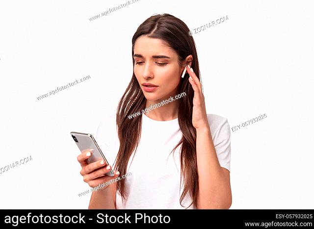 Close-up portrait of modern young woman in t-shirt, using wireless earphones listening music or podcasts, picking song in mobile phone