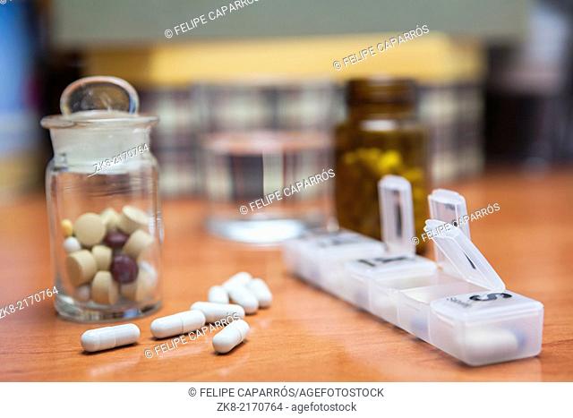 Old bottle of pills along with a few pills above a wooden table