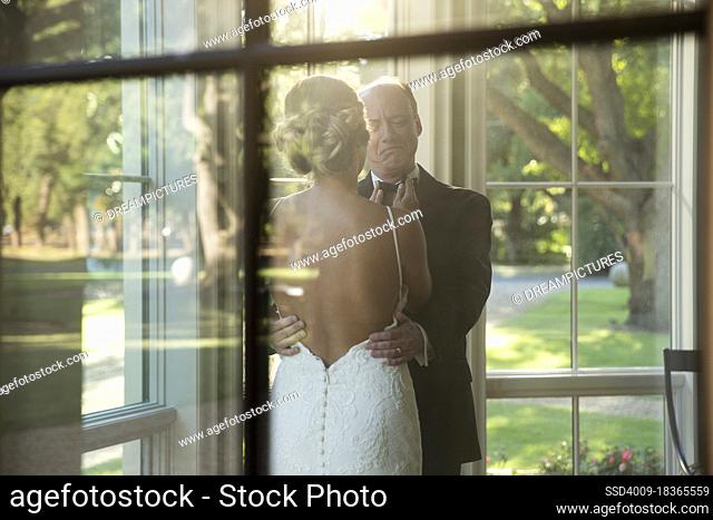 Bride fixing her fathers bow tie, seen through window
