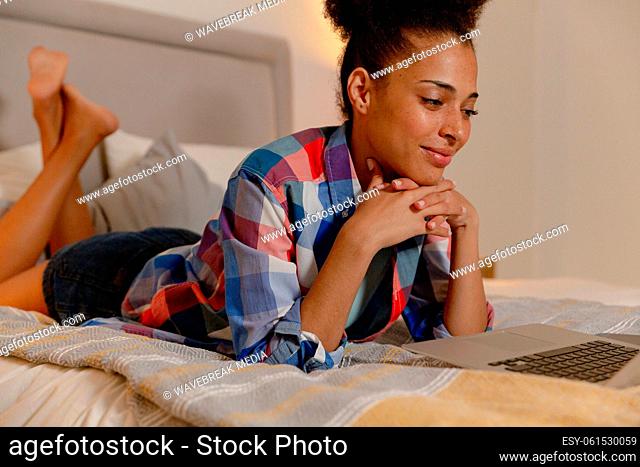 Mixed race woman lying in a bed using a laptop and smiling