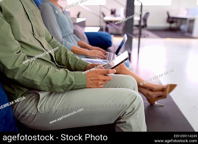 Midsection of male and female colleague sitting in office foyer using tablet and laptop