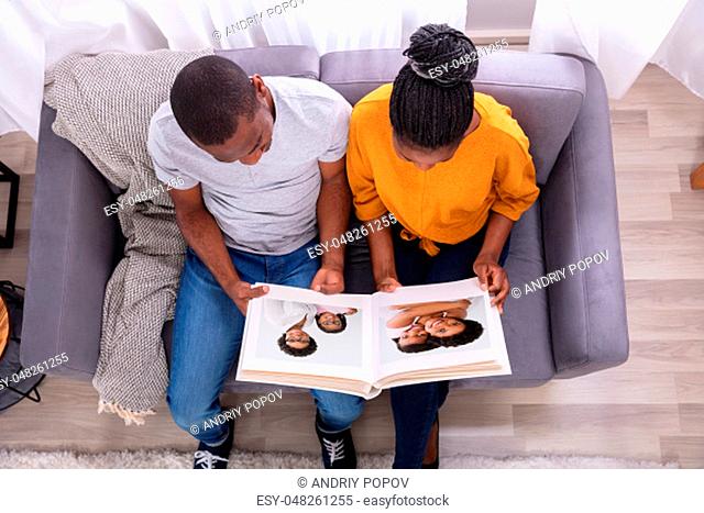 High Angle View Of An African Couple Sitting On Sofa Looking At Photo Album