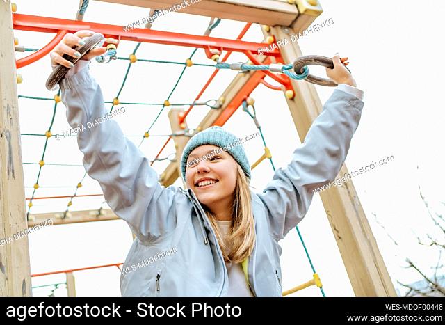 Smiling teenage girl playing on playground under sky