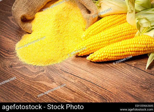 Ripe young sweet corn cob, on left stack cornmeal on wooden background, copy space.Gluten free food concept