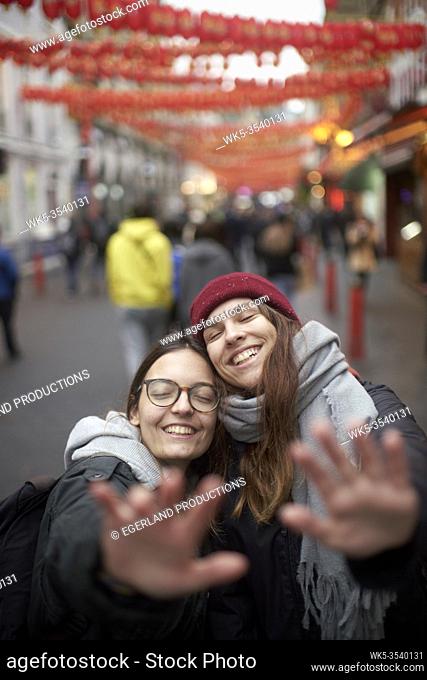 two women enjoying inner world together and keeping distance with hands between passersby in China Town in London, Great Britain