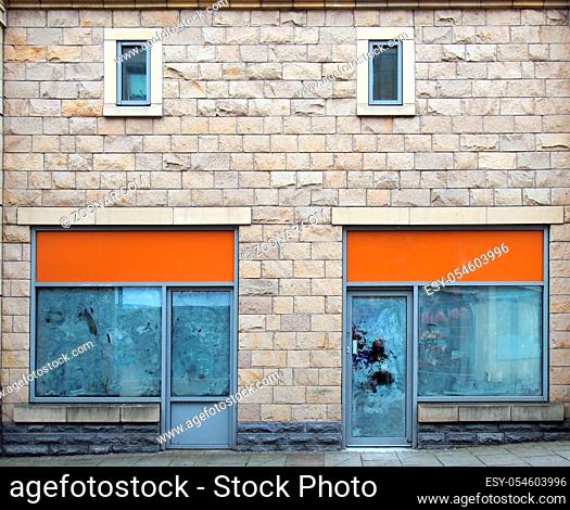 two empty abandoned shops on a street with whitewashed empty windows and blank store signs