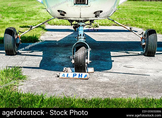 Small single engine old airplane wheels and landing gear on parking pad with wheel chocks on sunny day