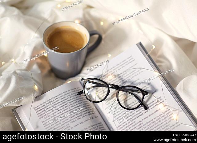 cup of coffee, book, glasses and garland in bed