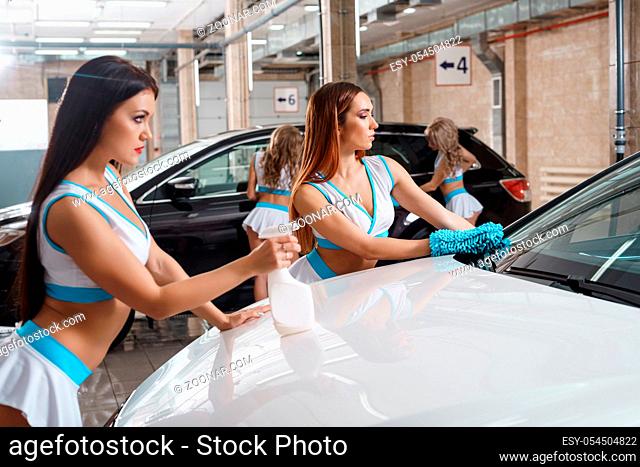 Sexy long haired girls in formula one style tops and mini skirts posing with sprayers and sponges near car at carwash