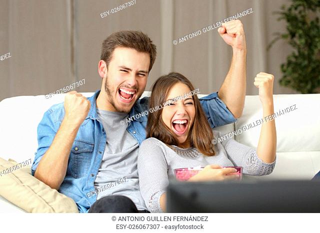 Euphoric couple watching tv sitting on a couch at home