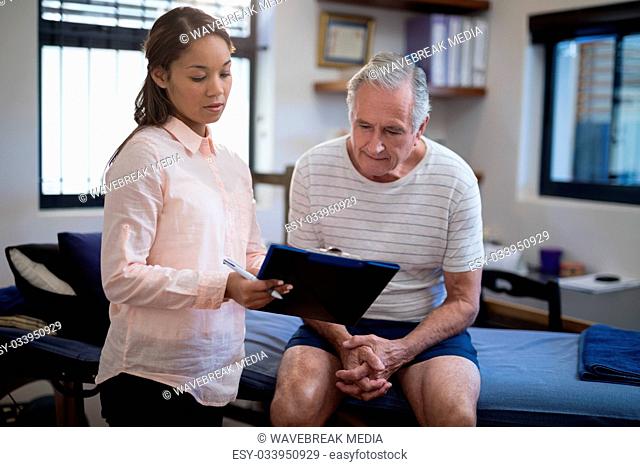 Female therapist showing clipboard to senior male patient sitting on bed