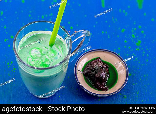 Close up of a glass of spirulina smoothie with a cup of spirulina on a blue background