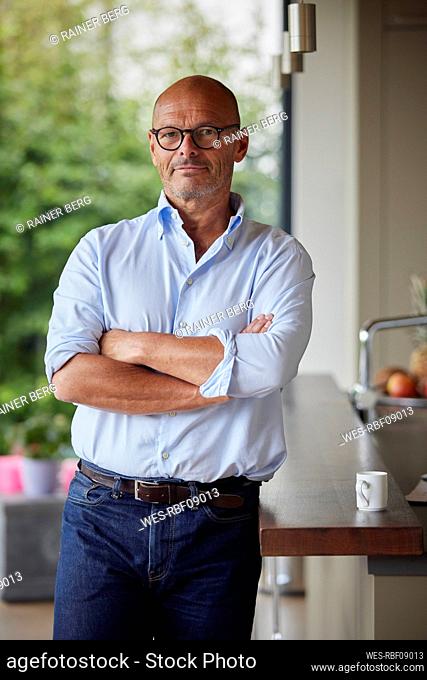 Senior man with arms crossed standing by kitchen island at home