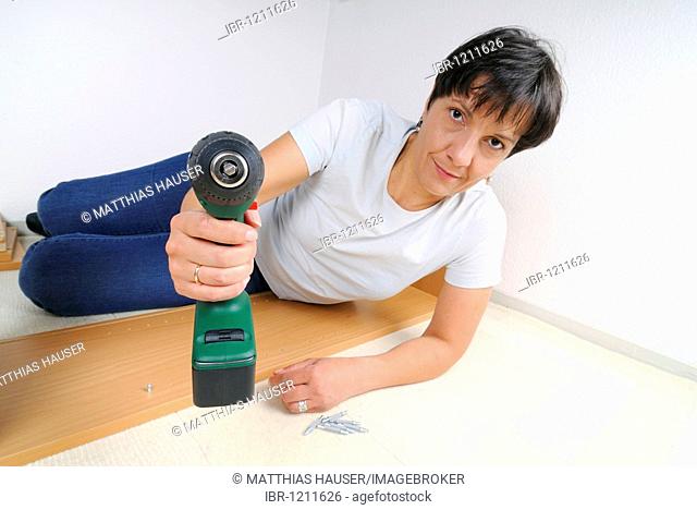 Woman with a cordless screwdriver assembling furniture