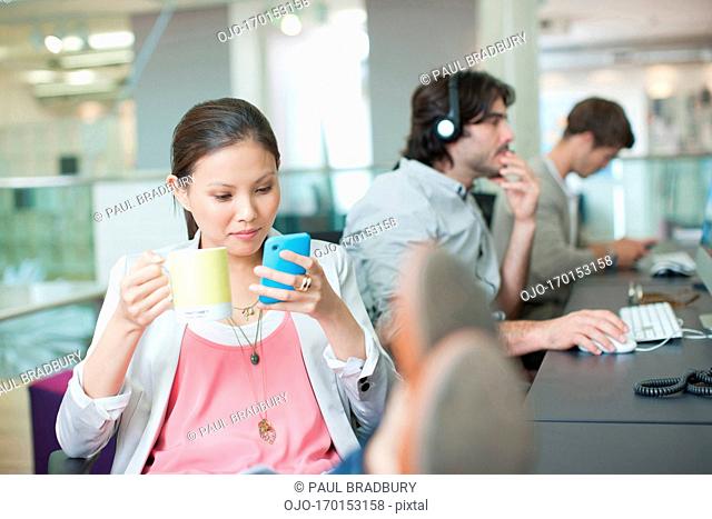 Businesswoman drinking coffee and text messaging with feet up in office