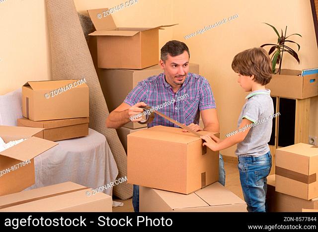Father packing things into boxes or cardboards and his son helping him. The whole family moving into a new house or apartment