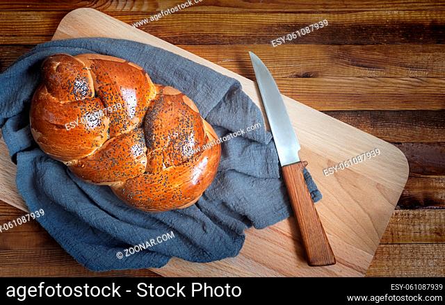 A loaf of white bread with a crisp crust, sprinkled with poppy seeds and a knife on the kitchen Board. Top view, copy space