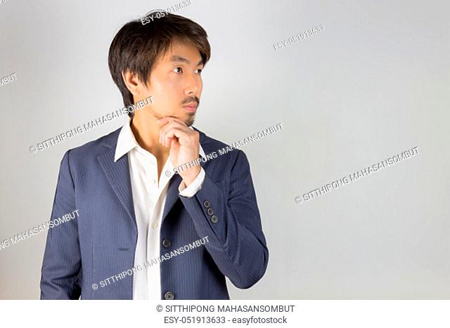 Portrait Man in Navy Blue Suit Looking Above and Touch Chin Pose. Portrait man in navy blue suit and white shirt on left frame of grey background in smart style