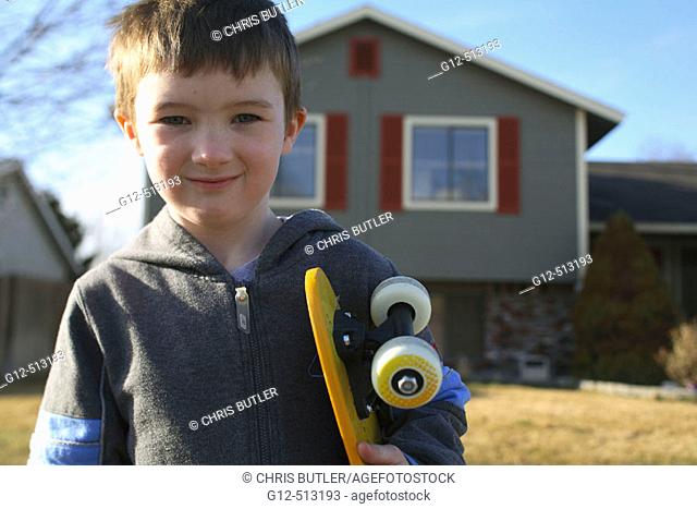 Boy, age five, looking at camera with skateboard in front of home