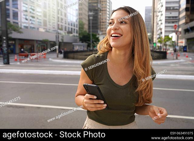 Laughing girl holding mobile phone looking to the side in empty metropolis avenue