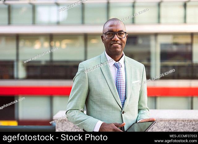 Smiling mature businessman with tablet PC standing in front of building