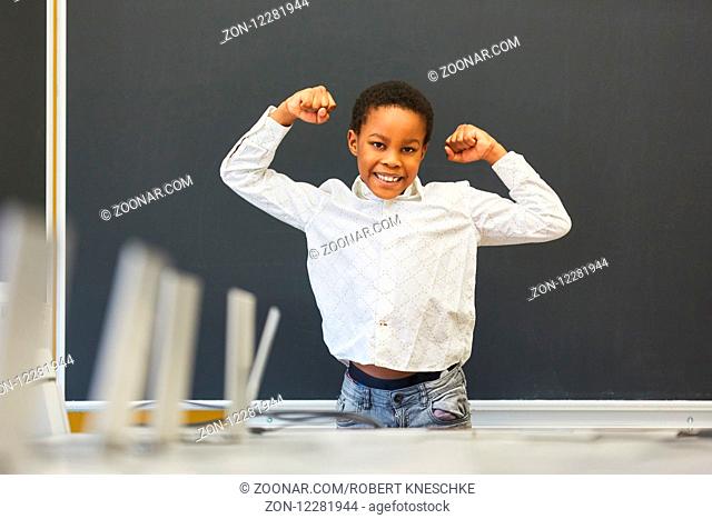 Selbstbewusster Schüler posiert als Sieger vor einer leeren Tafel in der Schule