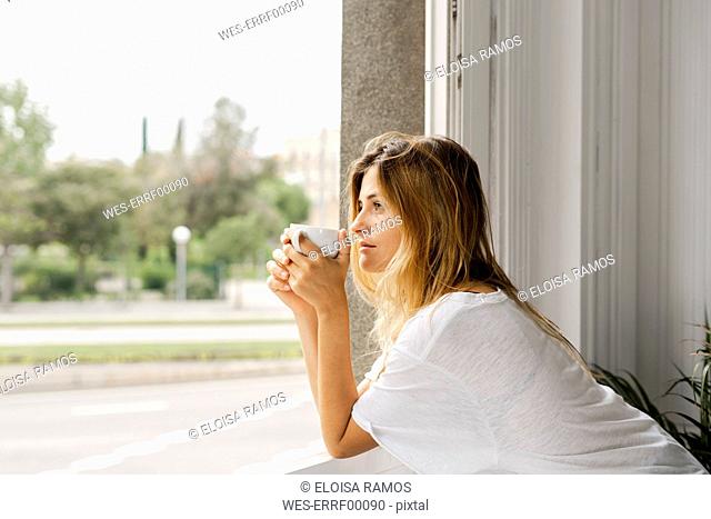 Young woman at the window holding cup of coffee