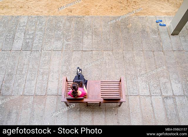a young woman with tablet computer sitting on a wooden bench on a plat, taken from above