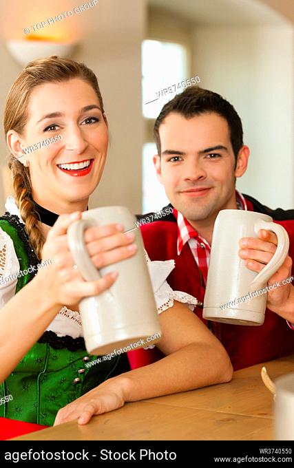 Young couple in traditional Bavarian Tracht in restaurant or pub with beer