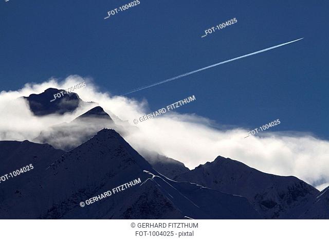 An airplane vapor trail over a mountain range, Graubunden Canton, Switzerland