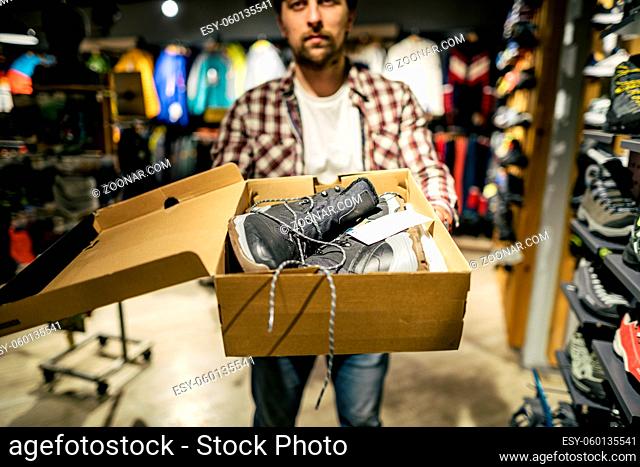 Store clerk helping customer try hiking boots at outdoors equipment shop. Salesman demonstrating trekking and hiking footwear for outdoor trails
