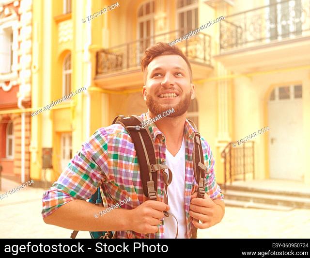 Portrait of smiling handsome man with packpack. Bearded man in plaid shirt walking in the city centre and enjoying his time. Toned image