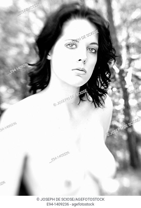Black and White portrait of a partially nude nineteen year old brunette woman looking at the camera in a forest setting