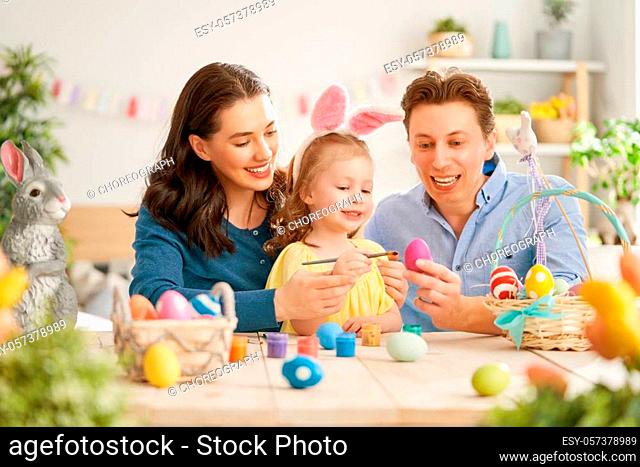 Mother, father and daughter are painting eggs. Happy family are preparing for Easter. Cute little child girl wearing bunny ears