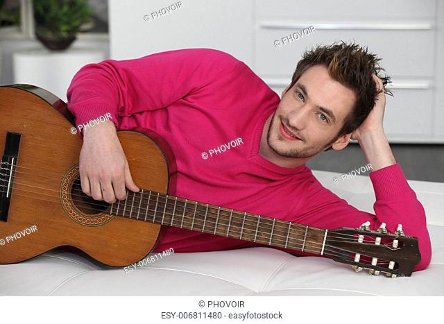 Man laying on sofa with acoustic guitar